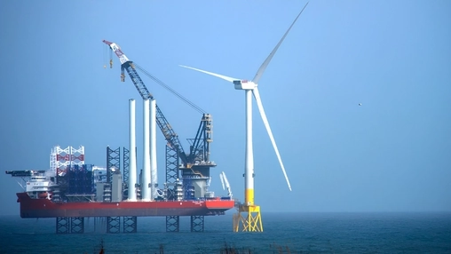 Red and white offshore installation vessel with crane alongside a wind turbine on a yellow monopile at sea