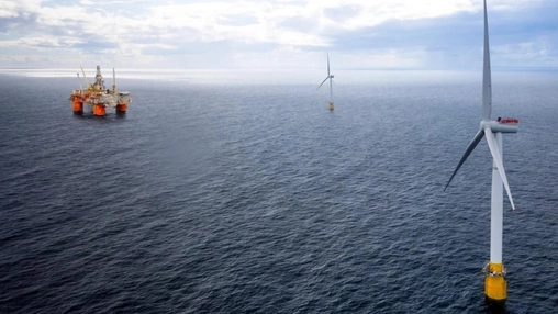 Large floating offshore wind turbine in the foreground with an oil and gas platform visible in the distance