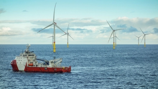 Red offshore supply vessel sailing near five offshore wind turbines with yellow monopile bases in open water