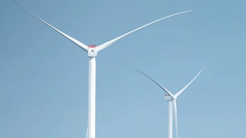 Two offshore wind turbines against a clear blue sky
