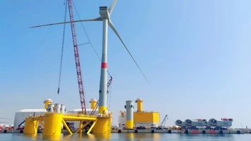 Floating offshore wind turbine on a yellow semi-submersible platform being assembled in port with a crane