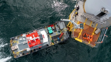 Overhead view of a red and white crew transfer vessel docked at an offshore wind turbine access platform
