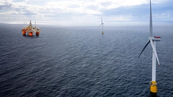 Large floating offshore wind turbine in the foreground with an oil and gas platform visible in the distance