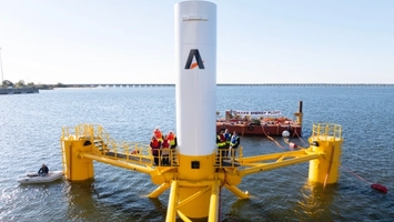 Engineers in high-vis vests on a yellow floating offshore platform with a white branded turbine tower