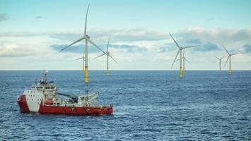 Red offshore supply vessel sailing near five offshore wind turbines with yellow monopile bases in open water