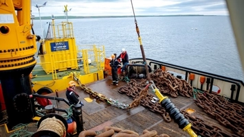 Workers in PPE managing rusted anchor chains beside yellow crane equipment on an IMEC offshore support vessel